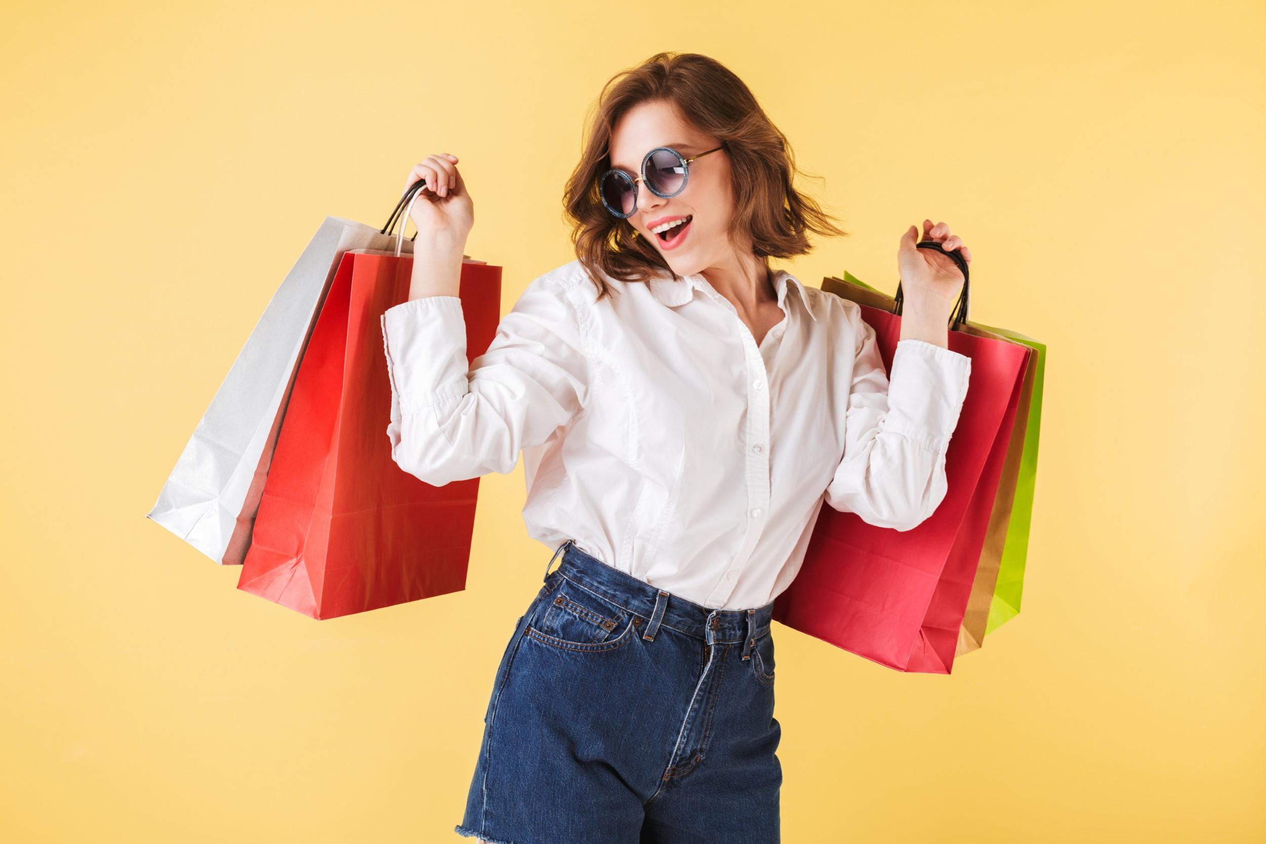 portrait happy lady sunglasses standing with colorful shopping bags hands pink background young woman standing white shirt denim shorts Stylistka